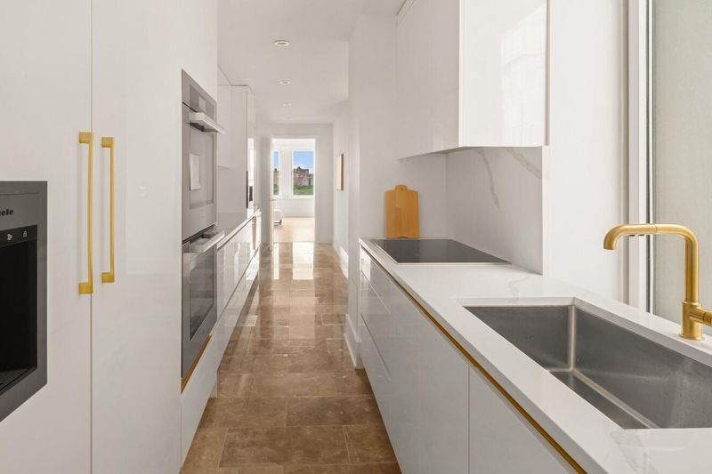Chef's kitchen, white custom cabinetry, integrated appliances, gold fixtures at 1200 Fifth Avenue 15A, Carnegie Hill — photo 4 of 13