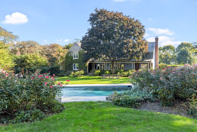 Lawn, pool and farmhouse behind the rose garden at 216 Sagaponack Road, Bridgehampton