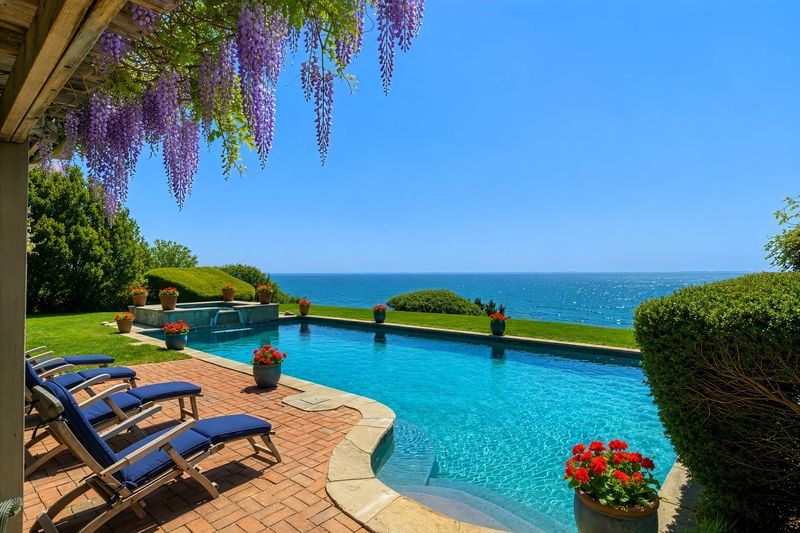 Waterside pool and brick terrace under a wisteria pergola, with Shinnecock Bay beyond at 24 Aqua Drive, Southampton