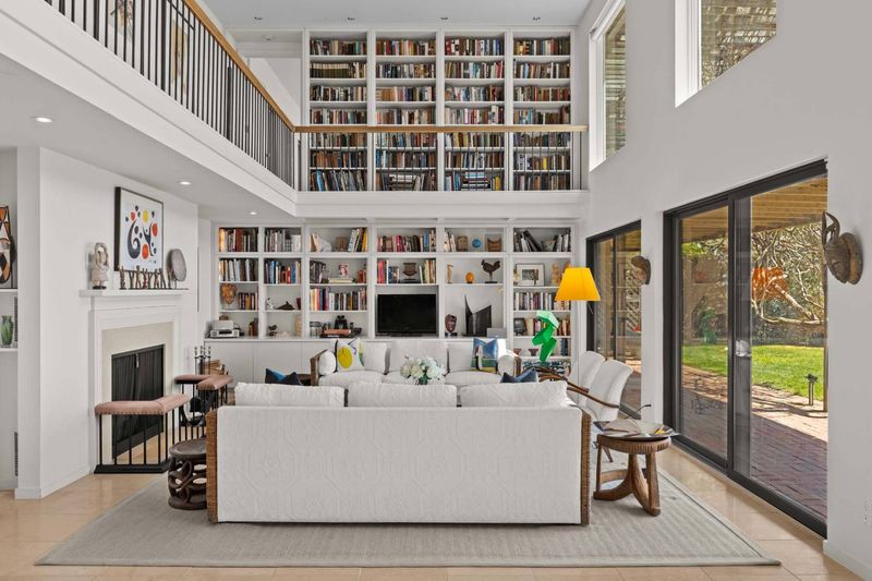Double-height living room with a two-story wall of bookshelves and a fireplace at 24 Aqua Drive, Southampton — photo 5 of 11