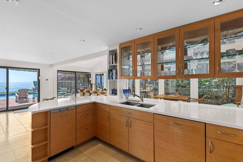 Kitchen with stone counters and wood cabinetry looking toward the pool at 24 Aqua Drive, Southampton — photo 8 of 11