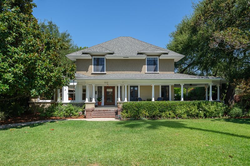 The Colonial Revival facade, with its deep wraparound porch, set back behind a broad front lawn and mature trees at 303 Markham Place, Pasadena