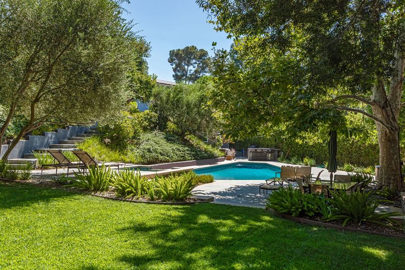 A broad lawn rolls down to the pool and chaise lounges, framed by mature trees at 3101 Fryman Road, Studio City