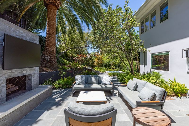 An outdoor living room with a fireplace and a mounted TV beneath the palms at 3101 Fryman Road, Studio City — photo 7 of 12