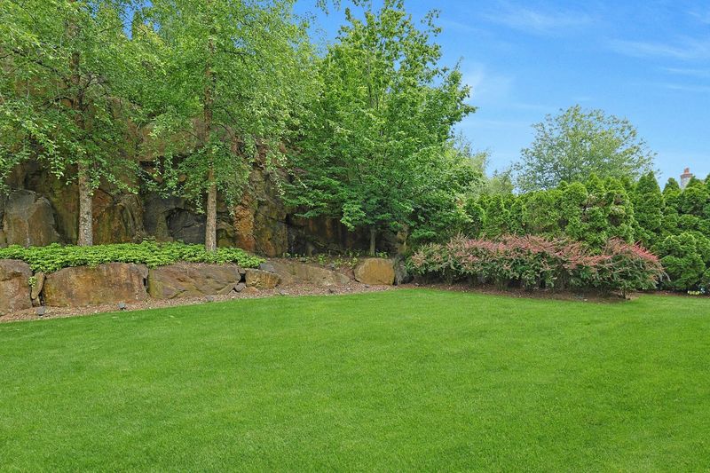 Level, grassy backyard framed by mature trees and stone walls at 5020 Iselin Avenue, Riverdale — photo 7 of 7