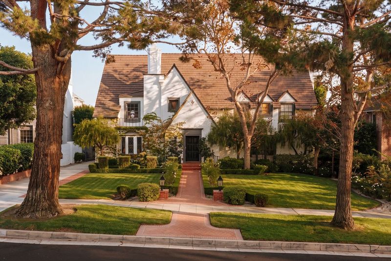 The Tudor Revival front facade behind a brick walk, lawn and mature trees at 628 North Sierra Drive, Beverly Hills