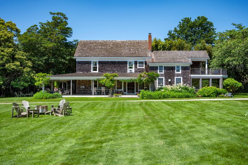 Shingled farmhouse and wraparound porch across the lawn at 645 North Sea Mecox Road, Southampton — photo 2 of 12