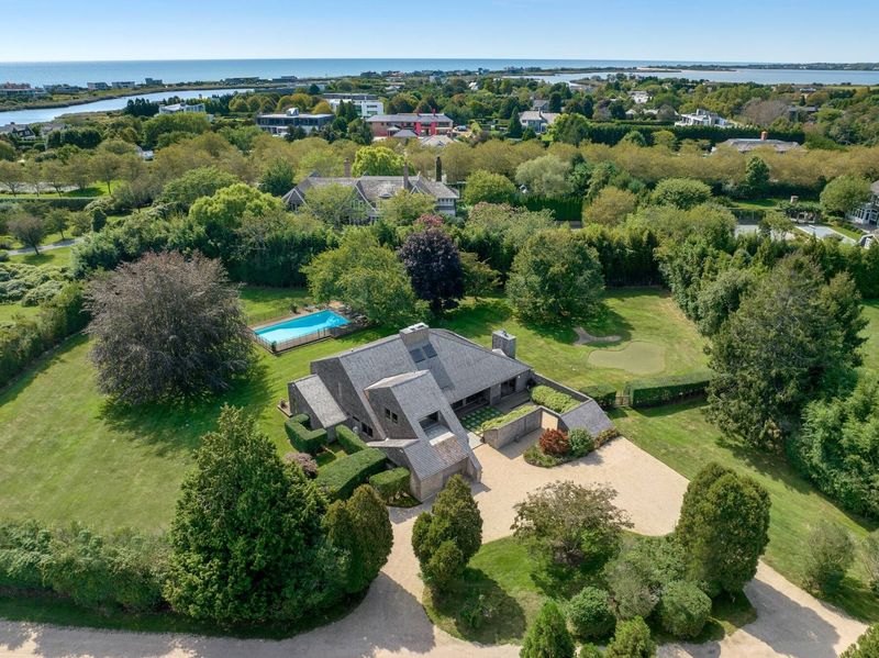 Aerial looking south: the house and pool set in a green, tree-ringed lot, with Bridgehampton's farmland and the Atlantic on the horizon. at 95 Jobs Lane, Bridgehampton — photo 2 of 12