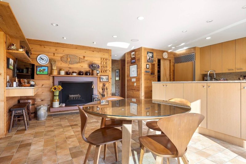The kitchen: a round glass breakfast table with bentwood chairs, a fireplace, light wood cabinetry and stone tile floors. at 95 Jobs Lane, Bridgehampton — photo 9 of 12